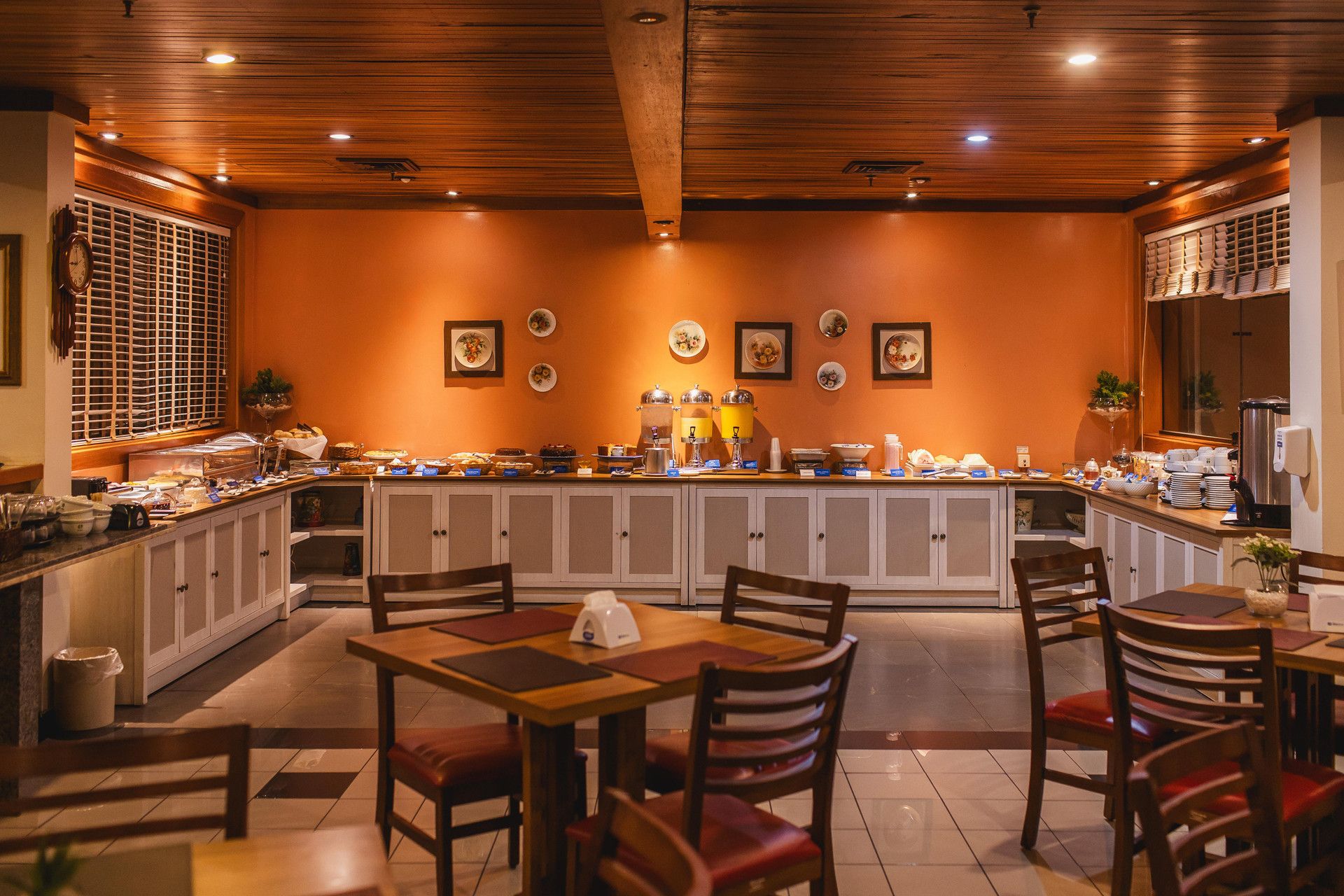 Un restaurante con techo de madera, un mostrador de buffet con diversos platos y una zona de estar con mesas y sillas.