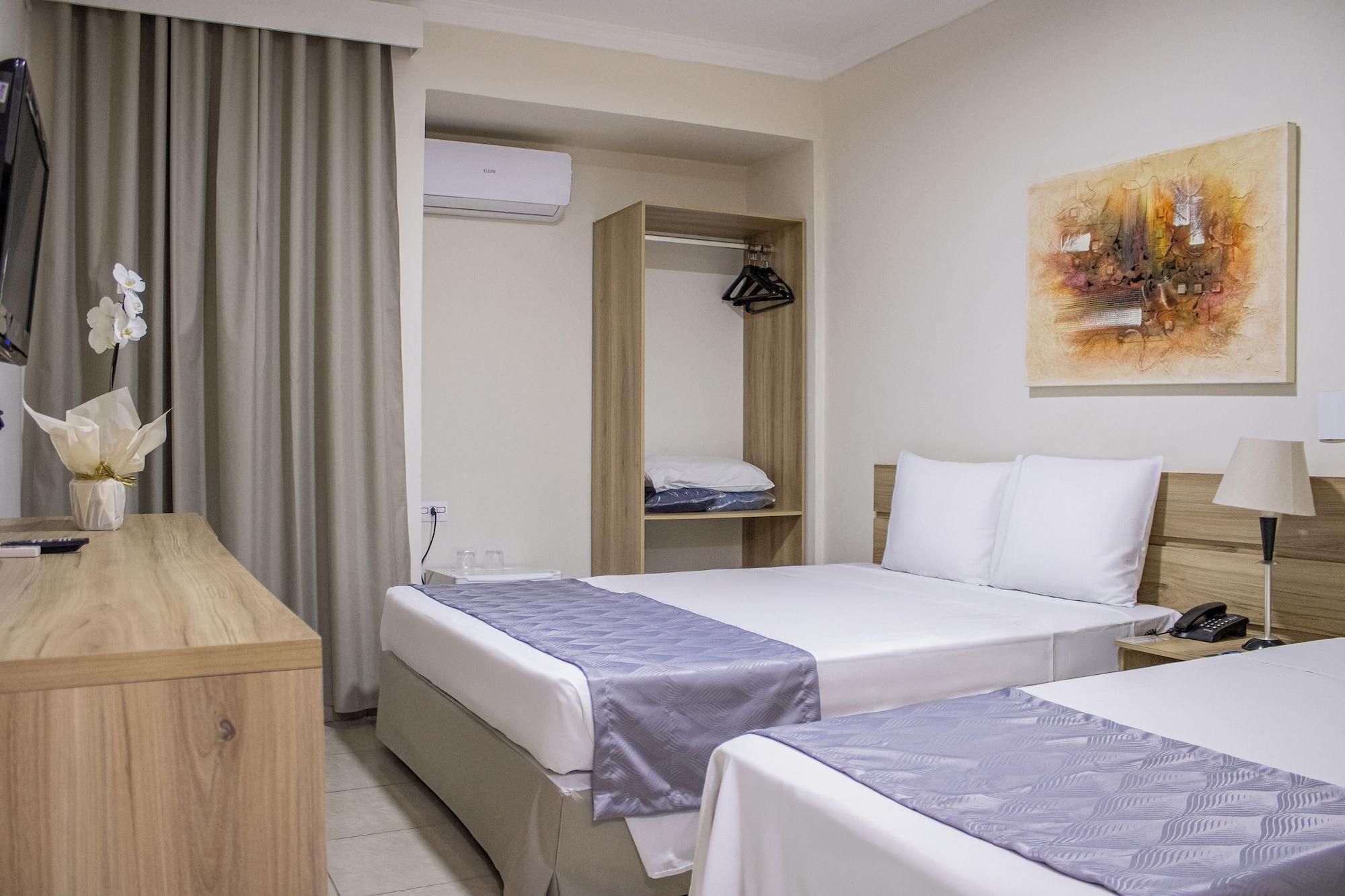 Habitación de hotel con dos camas, un escritorio de madera, un armario, un cuadro en la pared y un equipo de aire acondicionado.