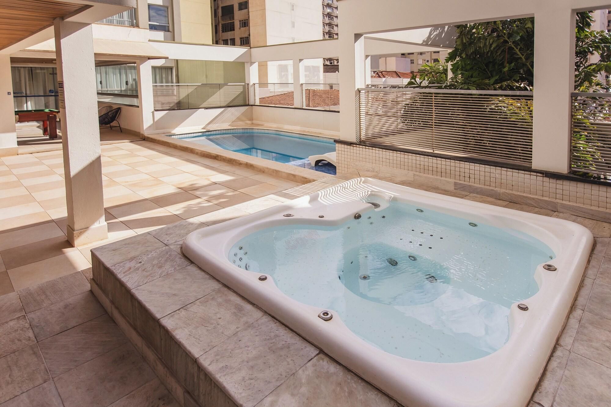 A hot tub and a swimming pool in an outdoor area with tiled flooring and a covered seating area.