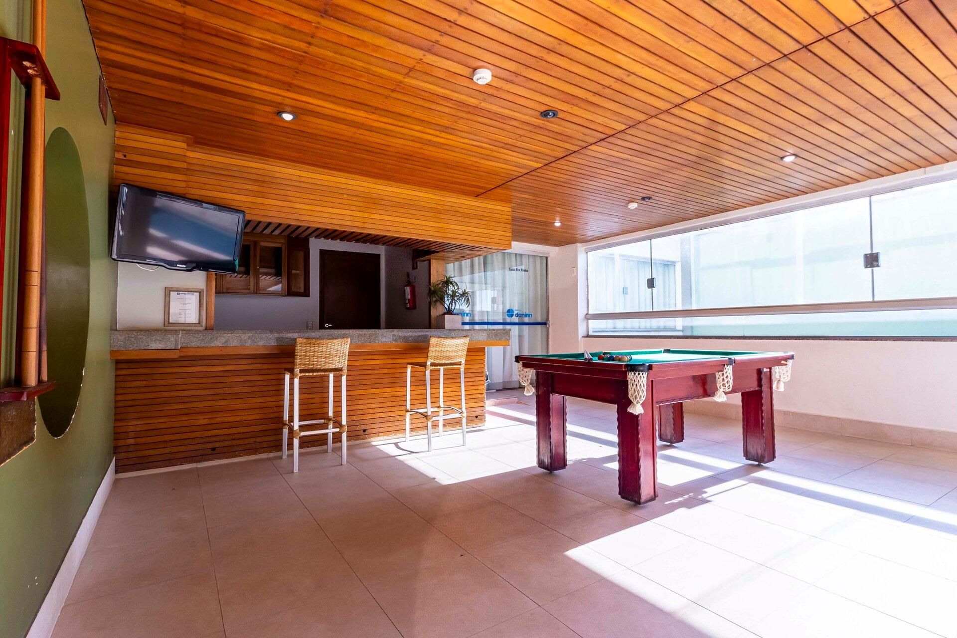 Una mesa de billar en una habitación con techo de madera y zona de bar.