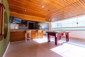 Una mesa de billar en una habitación con techo de madera y zona de bar.