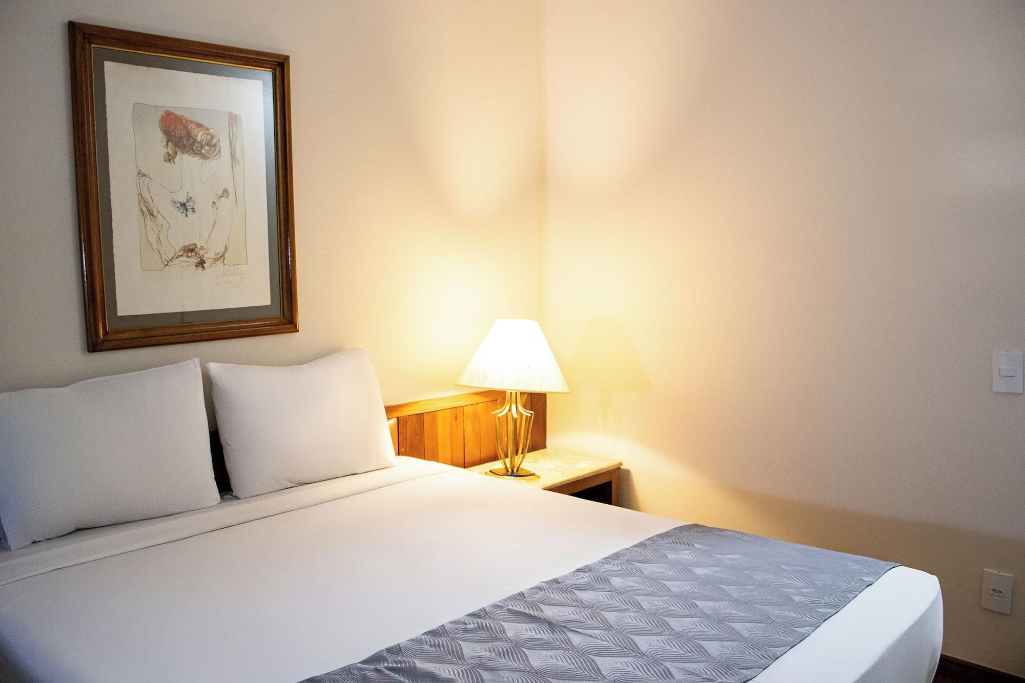 A hotel room with a bed, a nightstand, a lamp, and a framed artwork on the wall.