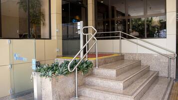 Entrada de hotel com porta de vidro, corrimão de metal e rampa de acesso.