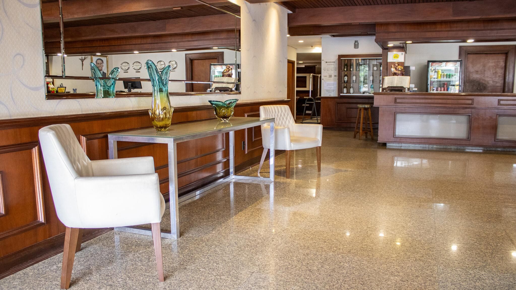 A hotel lobby with a marble floor, a reception desk, and two white chairs.