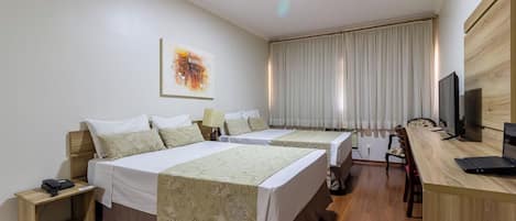 A hotel room with two beds, a desk with a computer, a television, and a window with curtains.