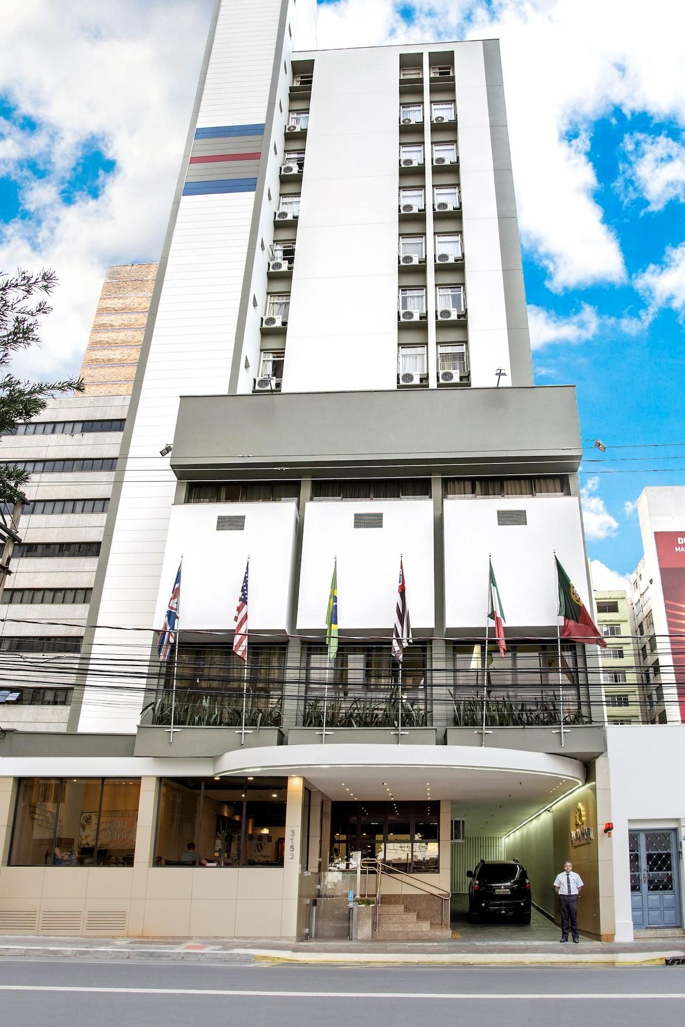 Un edificio moderno con varias banderas, un acceso cubierto y un coche estacionado en la entrada.