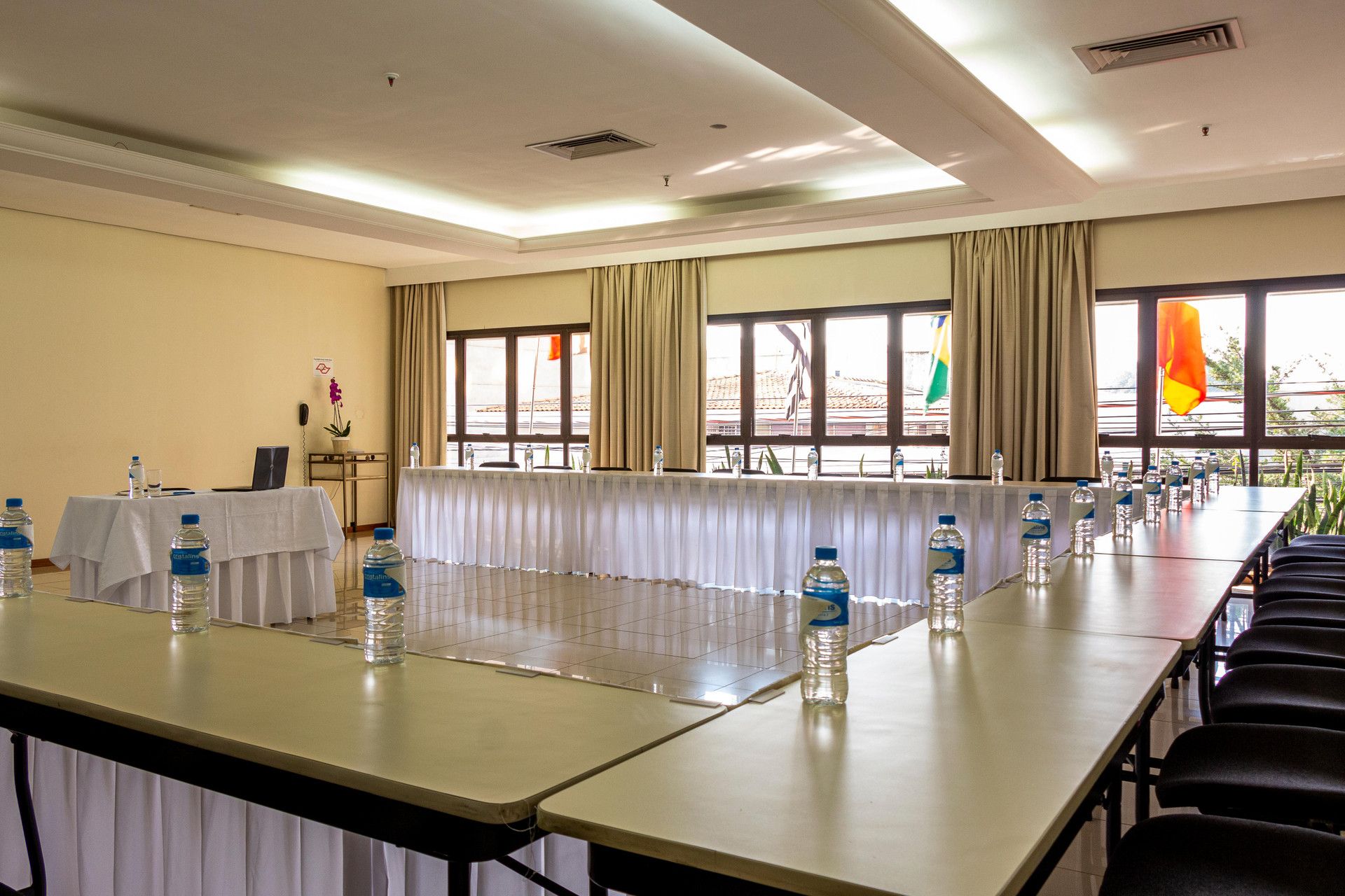 Un salón de conferencias con una larga mesa, sillas, botellas de agua y banderas.