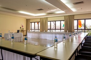 Un salón de conferencias con una larga mesa, sillas, botellas de agua y banderas.
