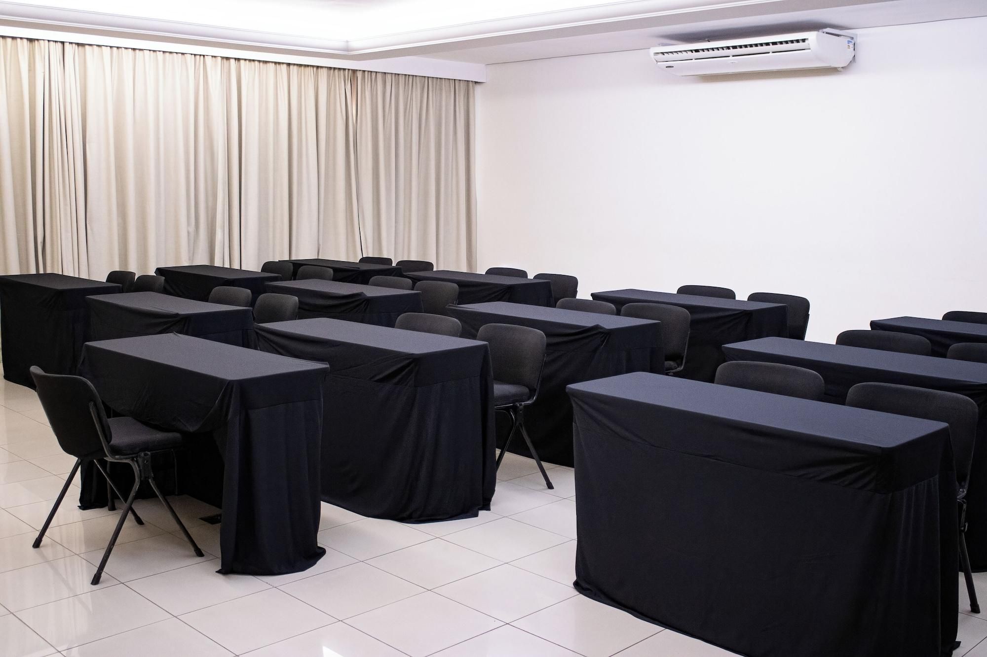 Uma sala de conferência com mesas, cadeiras, um ar-condicionado e uma cortina.