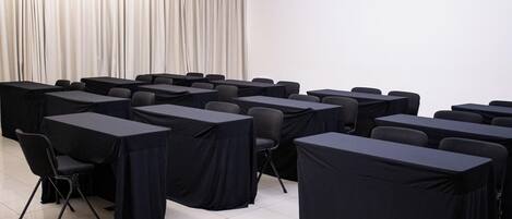 Uma sala de conferência com mesas, cadeiras, um ar-condicionado e uma cortina.