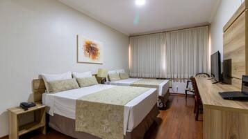 A hotel room with two beds, a desk, a television, and a large window with curtains.