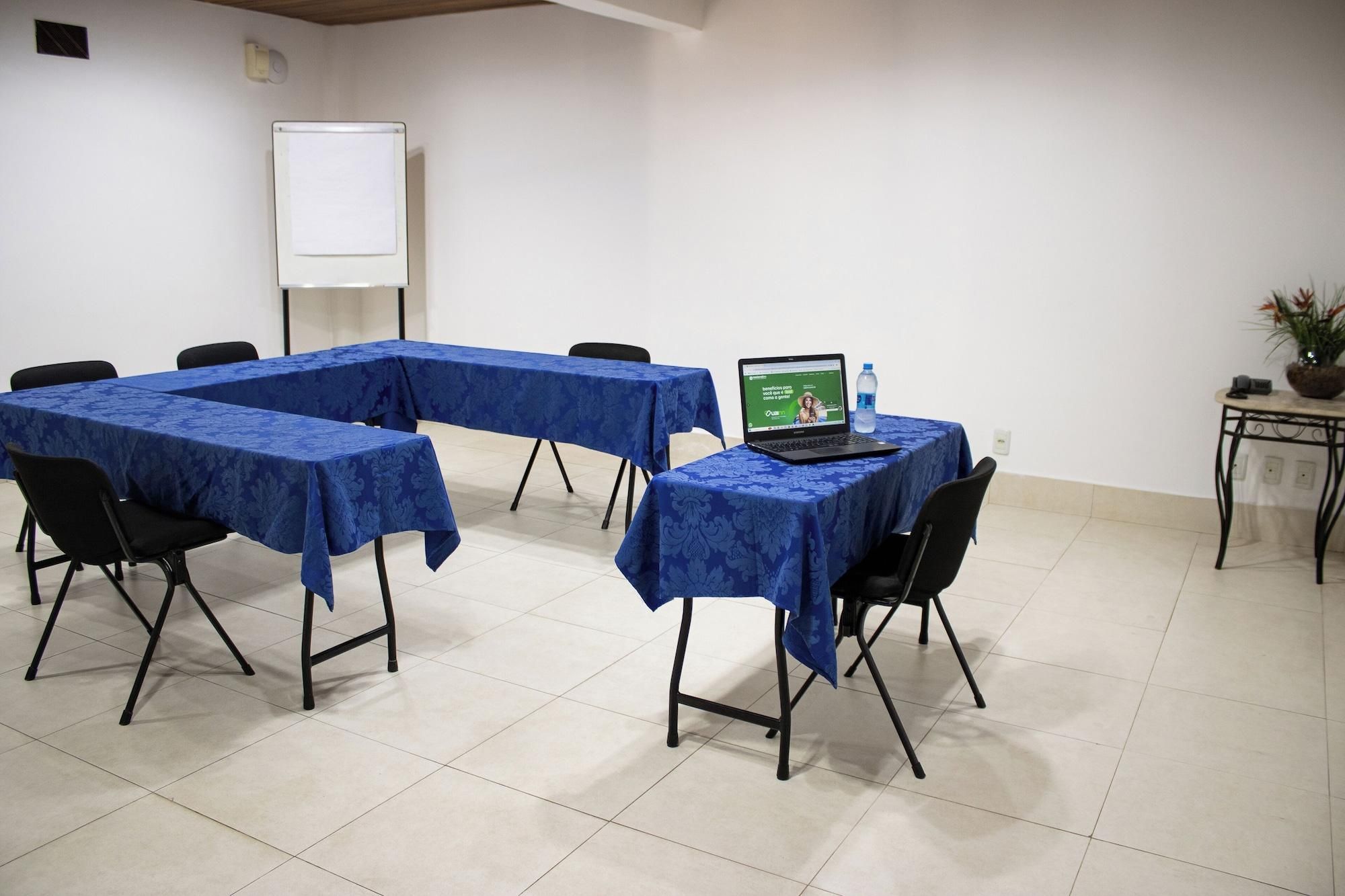 Una sala de conferencias con una pizarra, una laptop sobre una mesa y una planta en maceta.