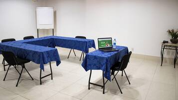 Una sala de conferencias con una pizarra, una laptop sobre una mesa y una planta en maceta.