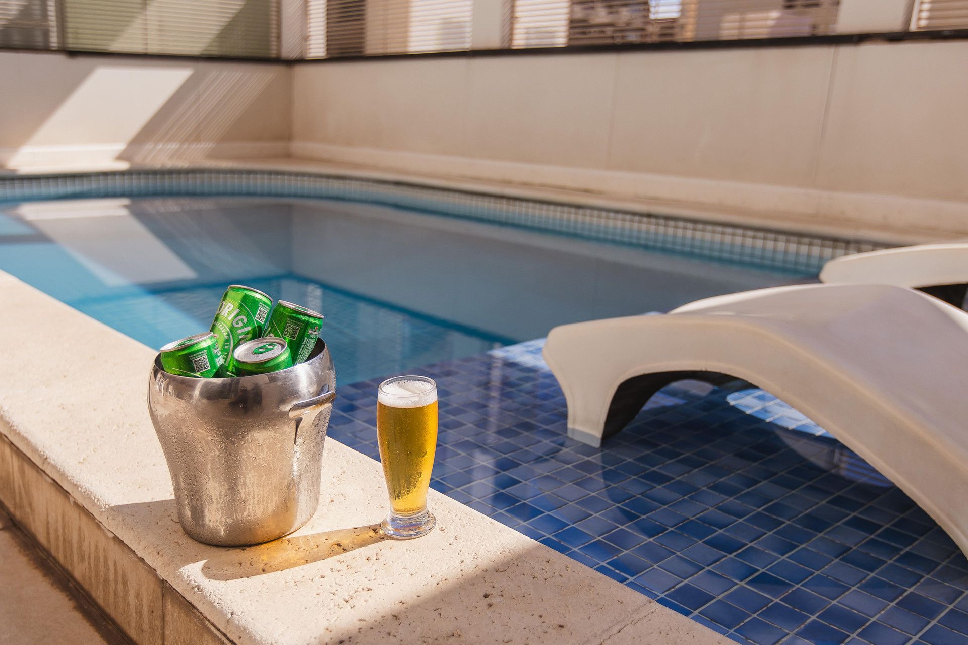 Ambiente à beira da piscina, com um balde de metal contendo latas e um copo de cerveja.