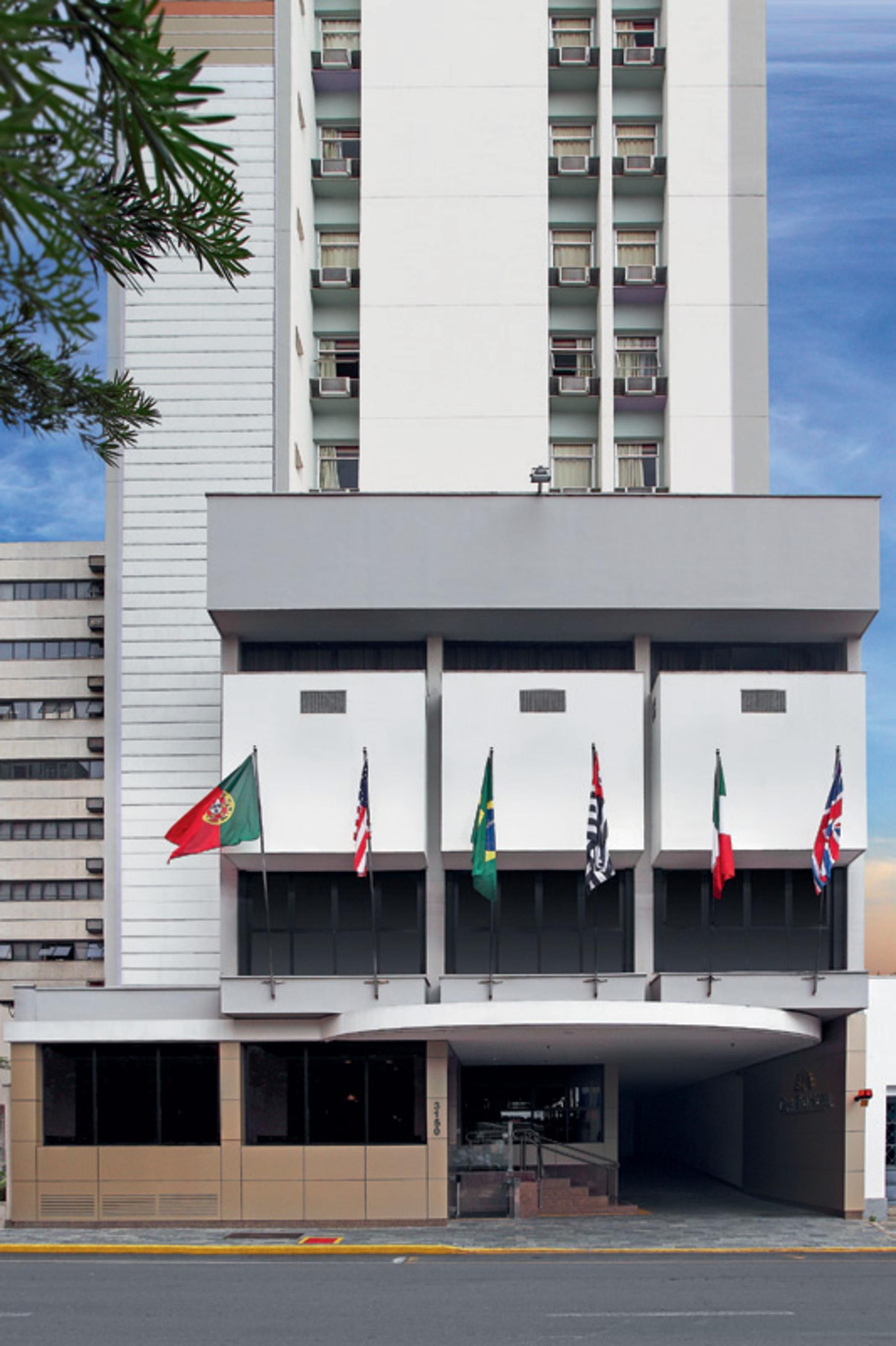 Un edificio moderno con fachada plana, varios balcones y una serie de banderas en la planta baja.