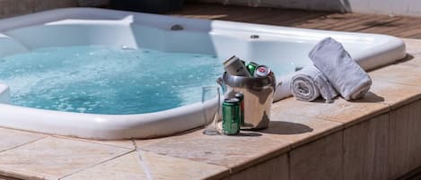 A hot tub with a metal bucket containing cans and a rolled towel on a tiled deck.