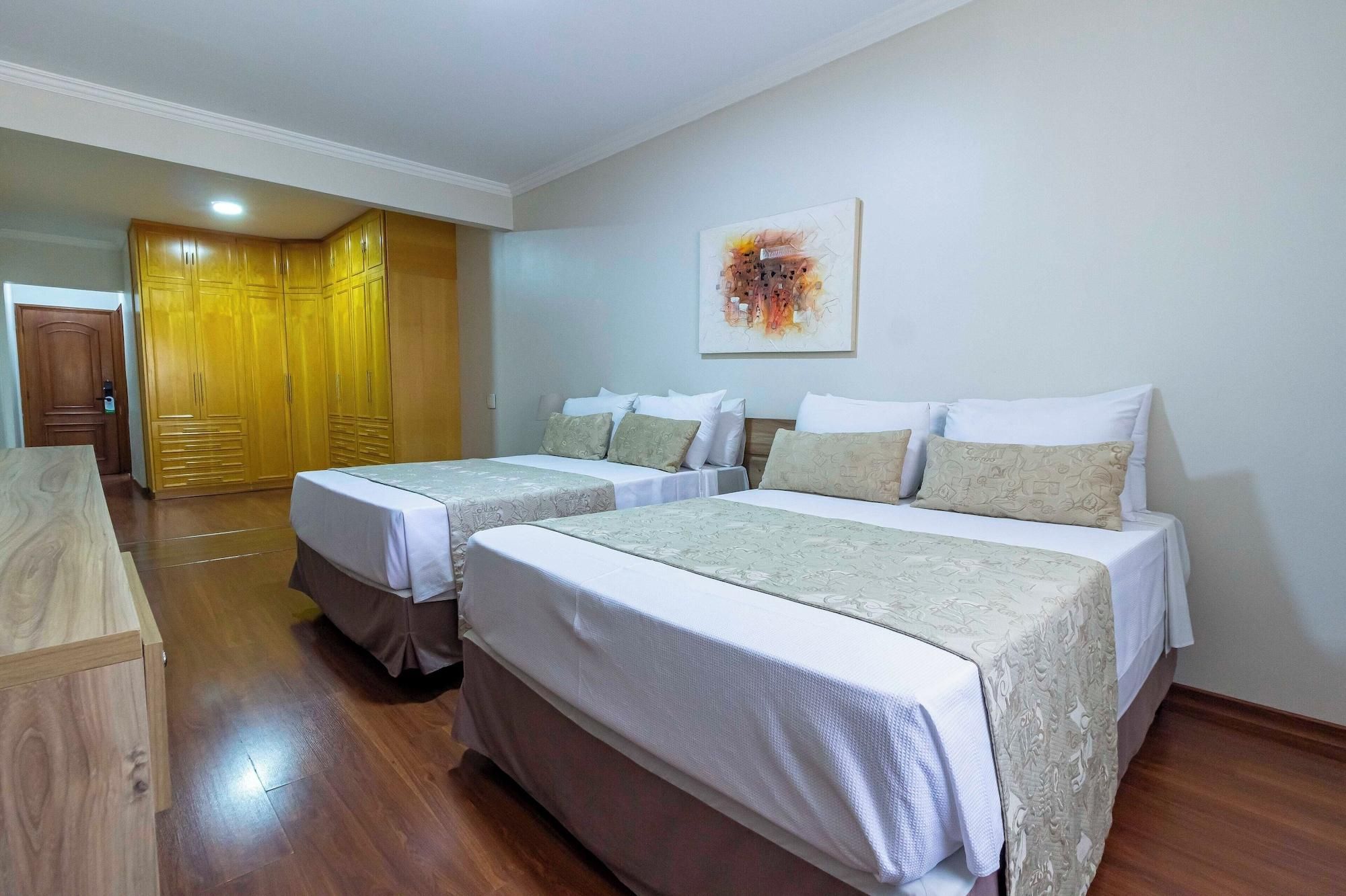 Una habitación de hotel con dos camas, un armario de madera, un cuadro en la pared y suelo de madera.