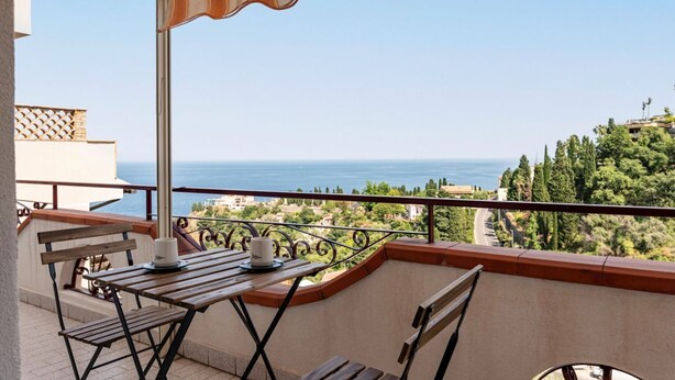 A balcony with a table, chairs, and a view of the sea.