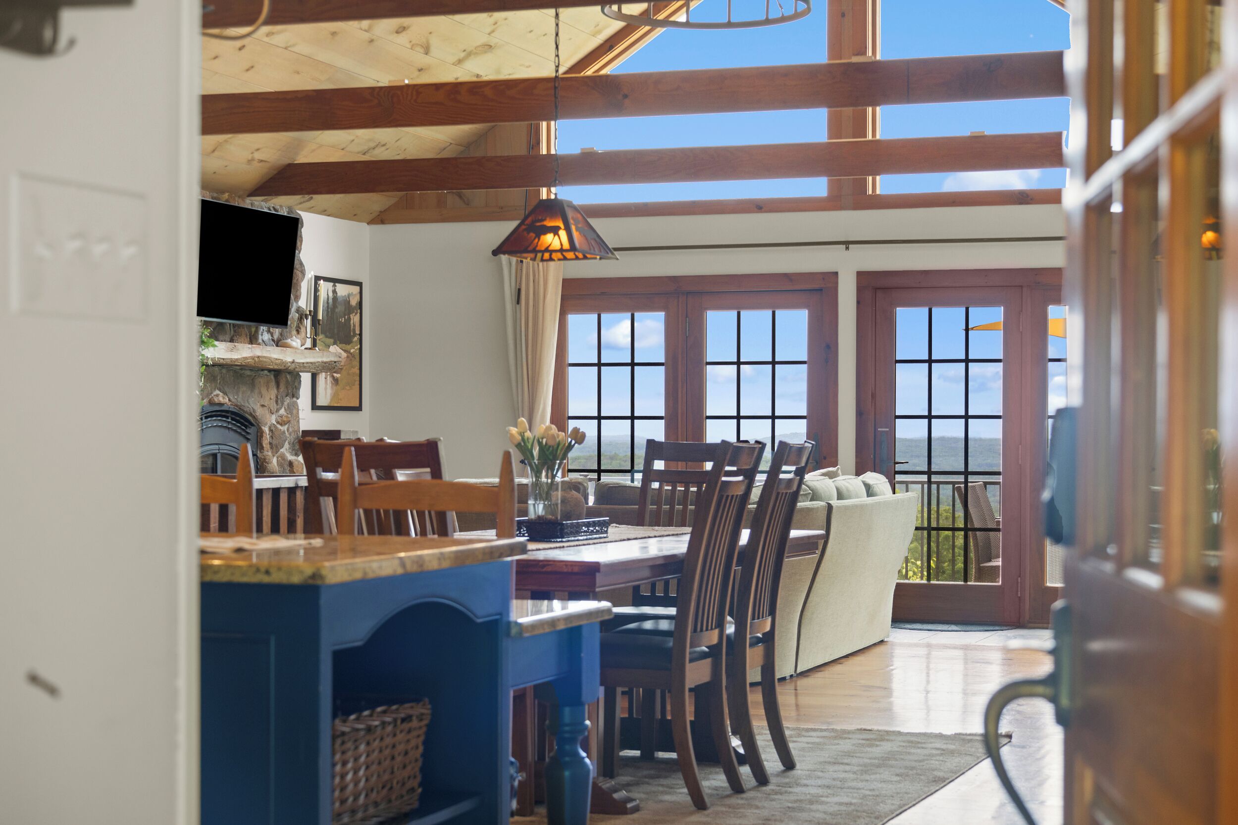Un espace repas avec une table et des chaises en bois, un comptoir bleu et une vue sur l’océan grâce à de grandes fenêtres.