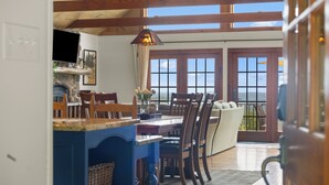 Un espace repas avec une table et des chaises en bois, un comptoir bleu et une vue sur l’océan grâce à de grandes fenêtres.