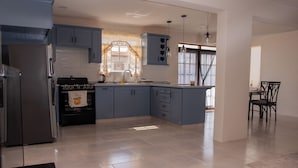 Une cuisine moderne avec des meubles gris, un réfrigérateur en acier inoxydable, une cuisinière à gaz et un coin repas comprenant une table et des chaises.