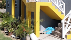 Un bâtiment à deux étages, à la façade jaune et grise, doté de balustrades blanches et d’un petit porche.