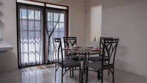 Un coin repas avec une table ronde et six chaises, une porte-fenêtre coulissante avec des rideaux et une petite fenêtre.