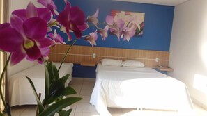 A hotel room with a bed, bedside table, and a wall with a floral painting. - Almeida's Hotel (Tangará da Serra)