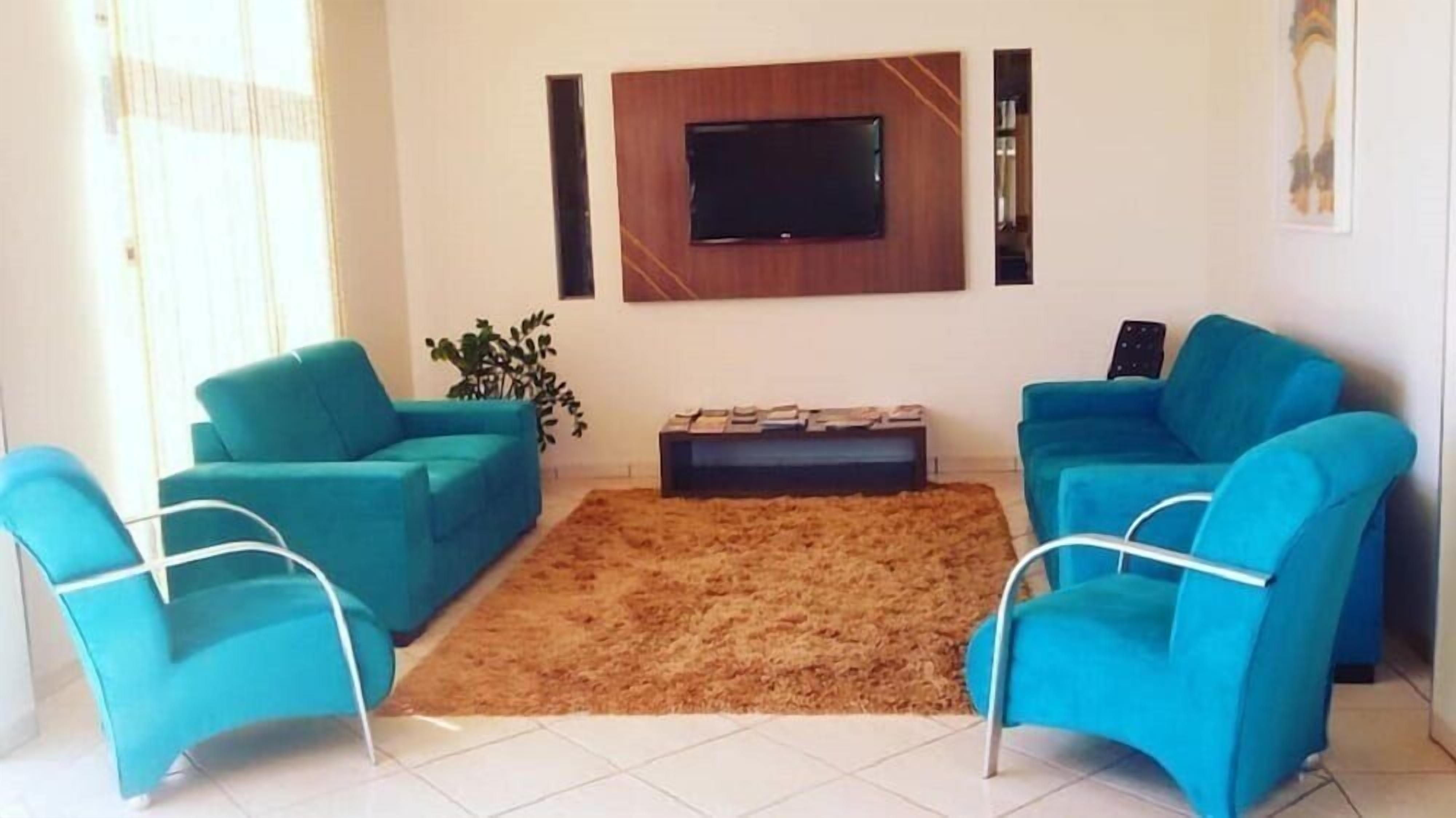 Sala de estar com dois sofás azuis, uma TV de tela plana na parede e uma mesinha com livros.