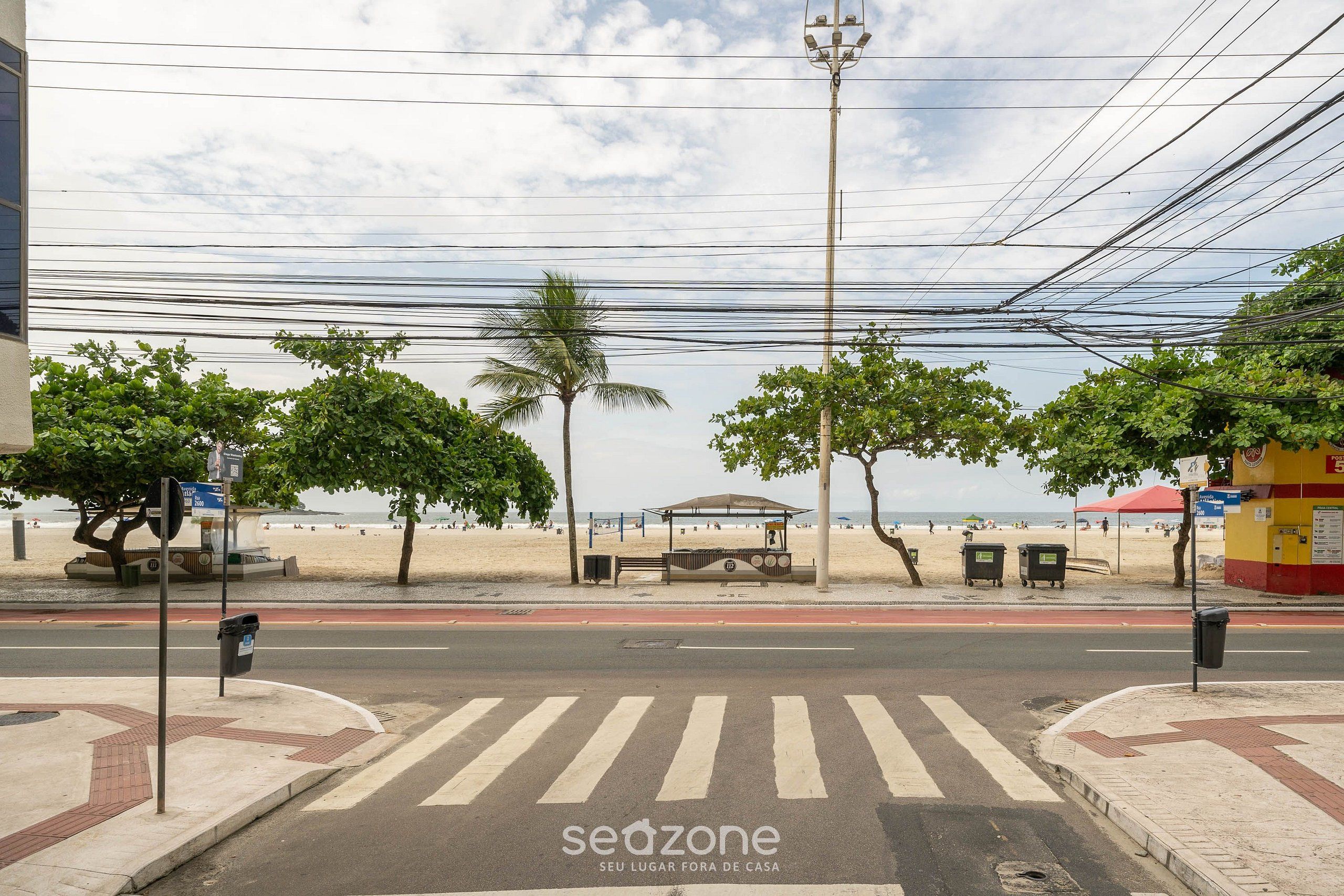 A beachside street with a pedestrian crossing, palm trees, and a beach in the background.