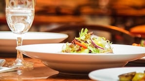 Taula de menjador amb un got d'aigua, un plat d'insalat i un plat blanc amb menjar.