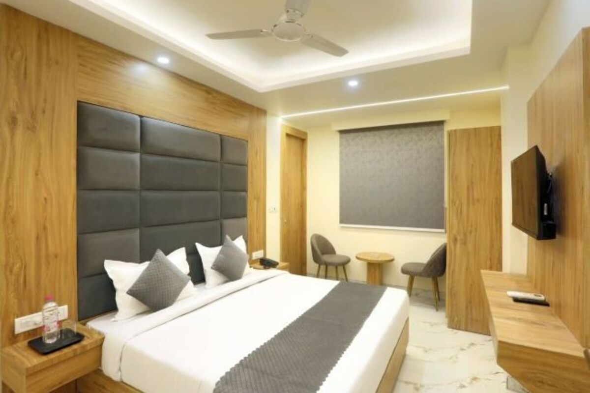 A modern hotel room with a large bed, a ceiling fan, a TV, a small table, and a chair.