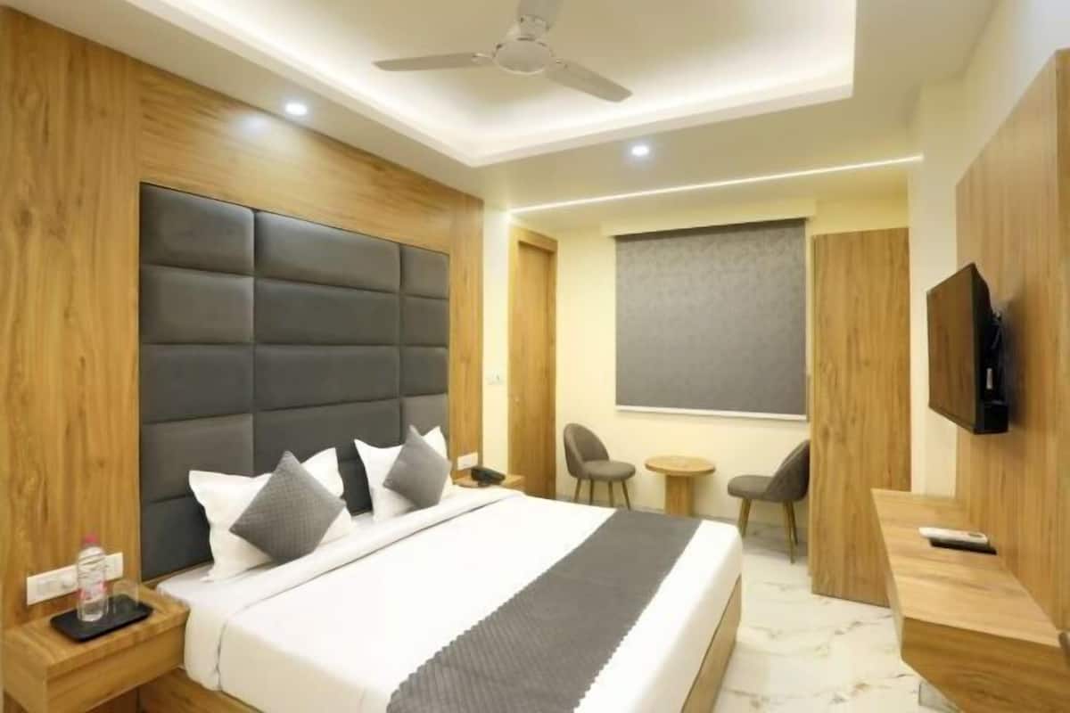 Una habitación de hotel moderna con una cama grande, un ventilador de techo, un televisor, una mesita pequeña y una silla.