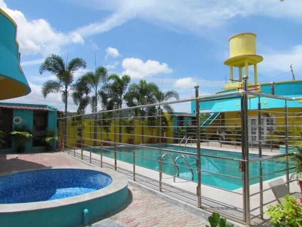 Una piscina con una cerca metálica, un depósito de agua y palmeras al fondo.