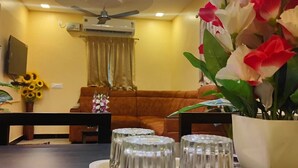Un salon avec un canapé marron, une table à manger avec de la vaisselle en verre transparent, un ventilateur de plafond et un climatiseur fixé au mur.