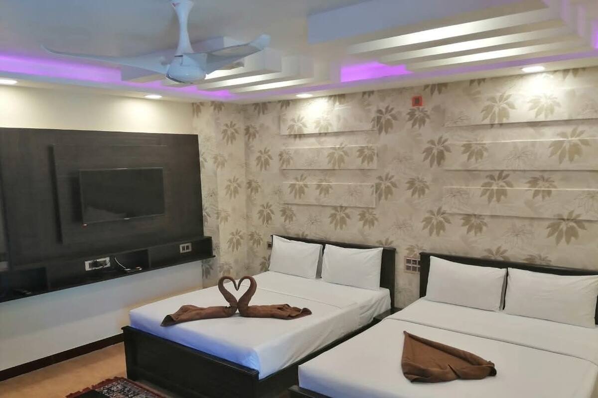 A hotel room with two beds, a flat-screen TV mounted on the wall, and a ceiling fan.