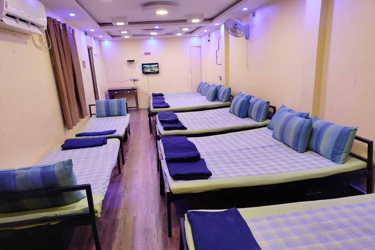 A hotel room with multiple single beds, each with a blue and yellow checkered bedspread and matching pillows. There is a television mounted on the wall, and the room has a wooden floor.