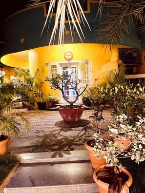 A courtyard with potted plants, a central tree, and a building with a yellow facade and a clock. - Star Resort (Mettupalayam)