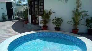 Une piscine dont le bord est recouvert de carreaux, entourée de plantes en pot et agrémentée d’une chaise.