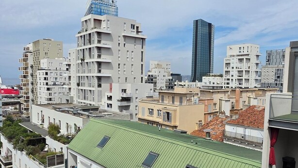 A multi-story building with a green roof, balconies, and a view of surrounding urban structures.