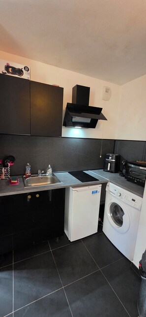 A compact kitchen with a sink, a compact washer, a microwave, and a black range hood. - Hotel contro Marsiglia (Marseille)