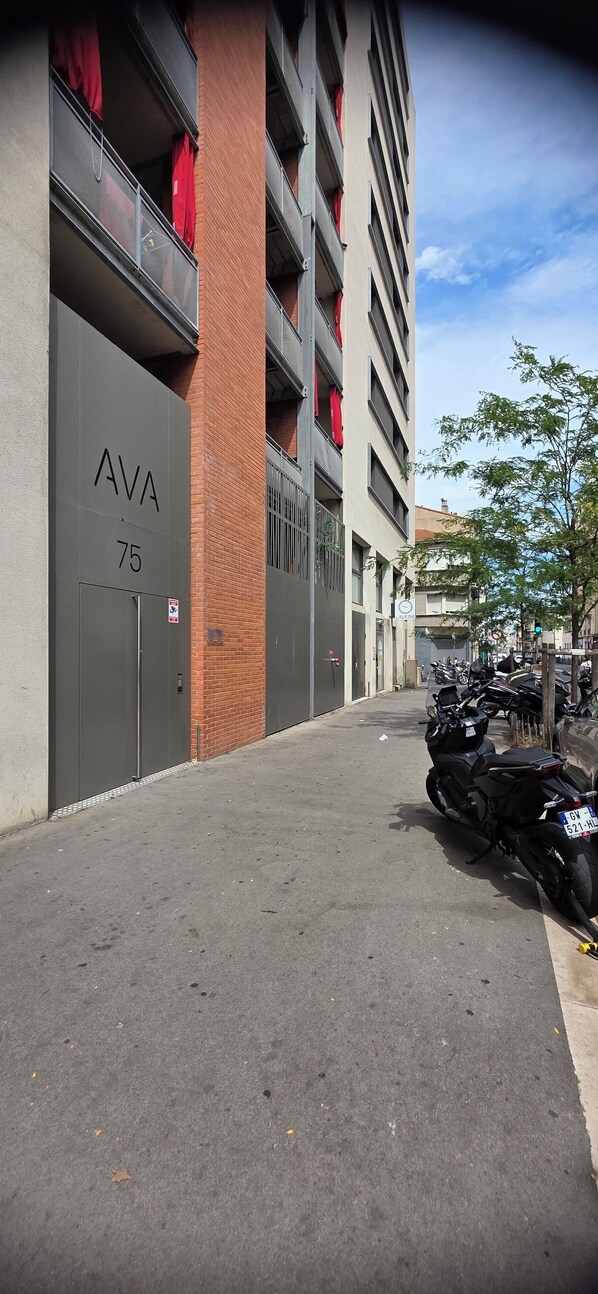 A multi-story parking garage with a grey facade, numbered parking bays, and a row of parked motorcycles.