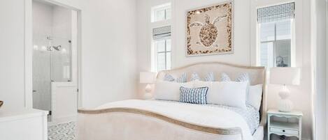 Un dormitorio con una cama grande, una mesita de noche, un velador, una obra de arte en la pared y una ventana con persianas.
