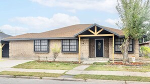 A two-story building with a brick facade, a black front door, and a small front yard with a tree and shrubs. - Downtown McAllen - Sleeps 10 (McAllen)