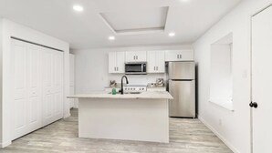 A modern kitchen with white cabinetry, a central island, a microwave, a stove, and a refrigerator. - Downtown McAllen - Sleeps 10 (McAllen)