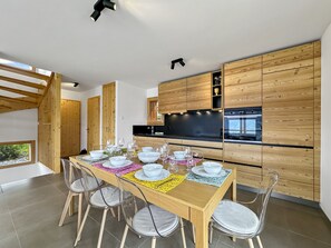 Een moderne keuken met houten kastjes, een eettafel gedekt met witte borden en glazen, en uitzicht op de omgeving.