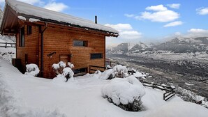 Une cabane en bois, dont le toit est recouvert de neige, se dressant sur un fond de montagnes.