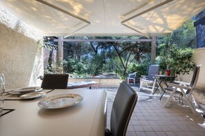 A covered patio area with a table set for dining, chairs, and a view of a garden.
