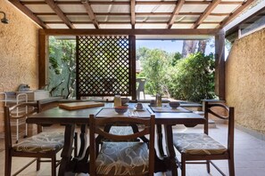 Une terrasse couverte avec une table à manger, des chaises et une vue sur la verdure.