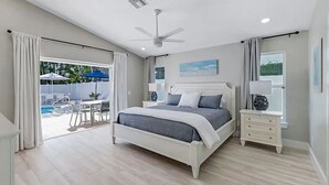 A bedroom with a bed, bedside tables, a ceiling fan, and a view of a swimming pool. - Coco Cobana - Heated Pool near Beach & Dining (Naples)